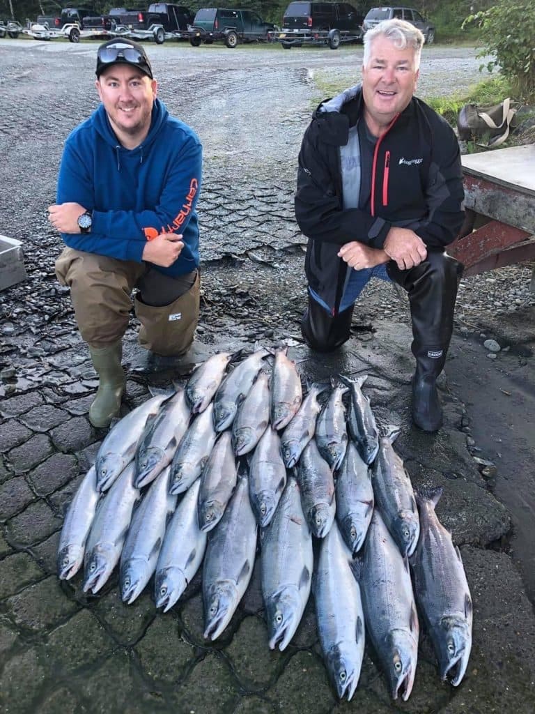 two men kneeling in front of a mountain of fish